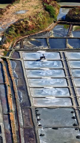 Single worker walks across rectangular salt pans at Plage des Océanides, viewed from above on a clear day.