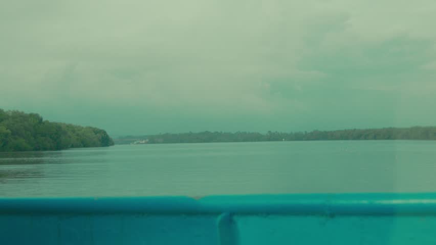 View from a boat moving along a calm river with forested banks under cloudy skies