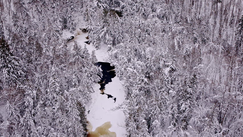 Aerial view of a forest and river blanketed in fresh snow across Northern Michigan.