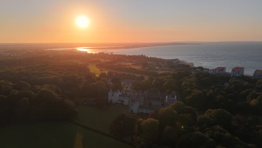 Cinematic aerial of Howth Castle overlooking Dublin Bay at colorful golden sunset
