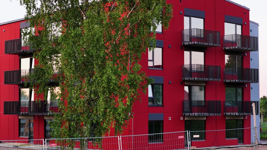 Newly built residential red building with modern architecture behind a construction fence