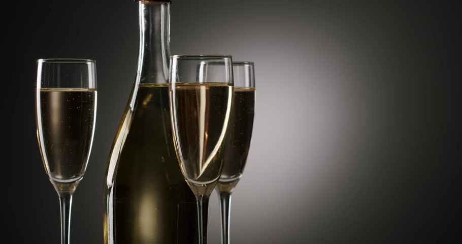 Elegant bottle of sparkling wine rotating with three glasses full of bubbling champagne on a dark, graduated background, symbolizing celebration, luxury, and a festive new year