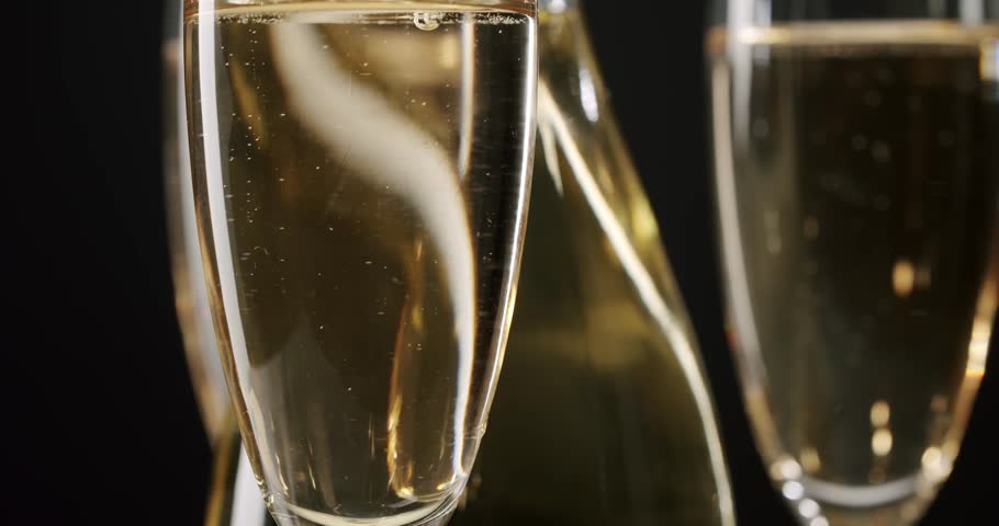 Elegant bottle of sparkling wine rotating with three glasses full of bubbling champagne on a dark, graduated background, symbolizing celebration, luxury, and a festive new year