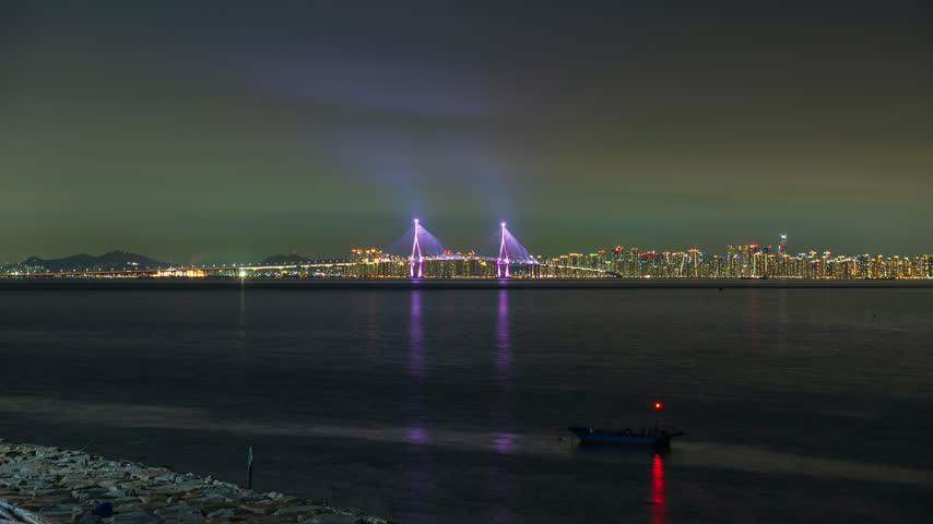 Timelapse Buck Moon and boat on the sea floats safely on top of the water with Incheon bridge buildings background. Lights from a passing airplane. South Korea.
