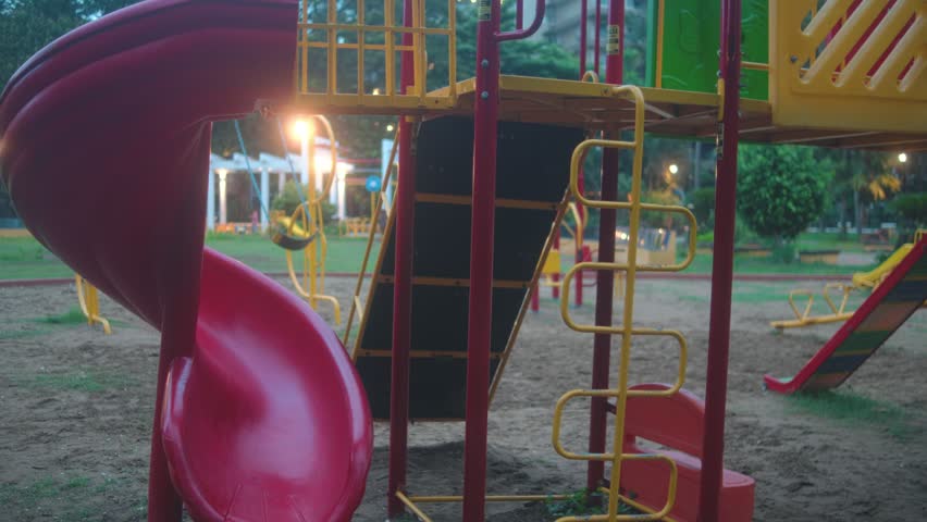 Colorful playground with slides, climbing structures, and play equipment in a public park during the early evening. Peaceful recreational space designed for children and families
