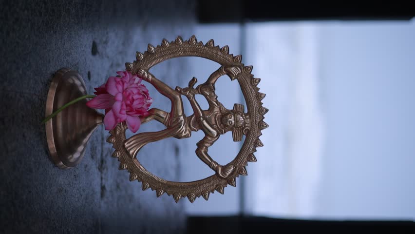 Bronze statue of Lord Nataraja Shiva adorned with fresh pink flowers.