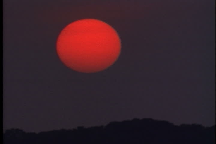 Big, red sun in purple dusky sky near sunset at Oyster Bay, Long Island, New York.