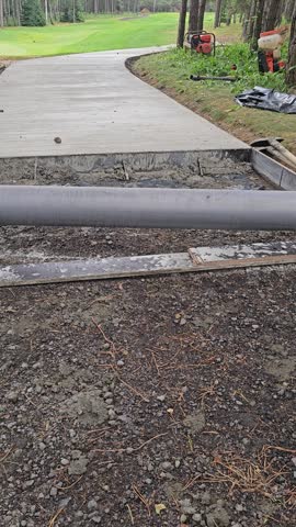 Work is in progress to create a new walkway in a park. Natural materials are used on site. Workers lay down forms and place cement for the surface.