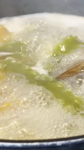 A close-up view shows colorful pasta ribbons submerged in bubbling boiling water inside a pot.