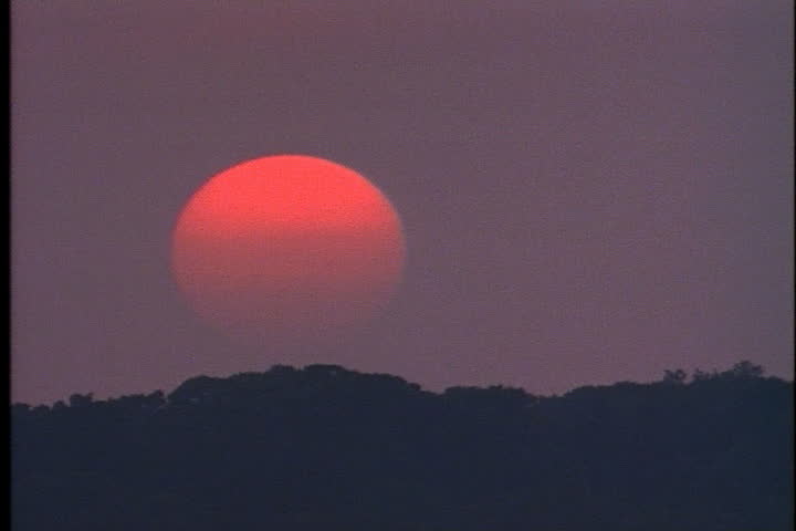 Big, red fireball sun sinking into purple sky at sunset at Oyster Bay, Long Island, New York.