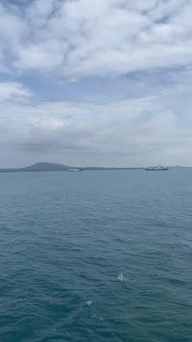 A serene seascape featuring a vast blue ocean under a cloudy sky, with distant mountain ranges and small vessels visible on the horizon during a voyage.