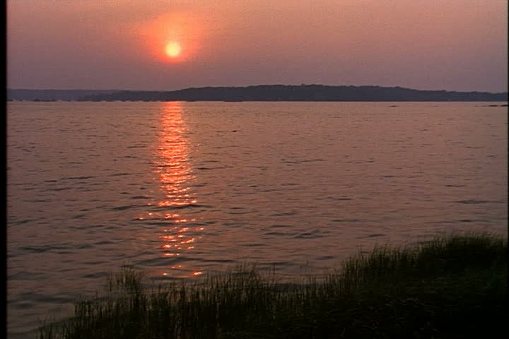 Orange sunset reflecting on surface of water in Oyster Bay, Long Island, New York.