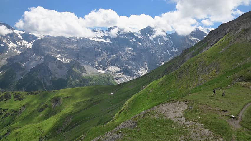 Dramatic Swiss Alps landscape with snow-covered mountains, vivid green slopes, rocky ridges and drifting summer clouds near Birg.