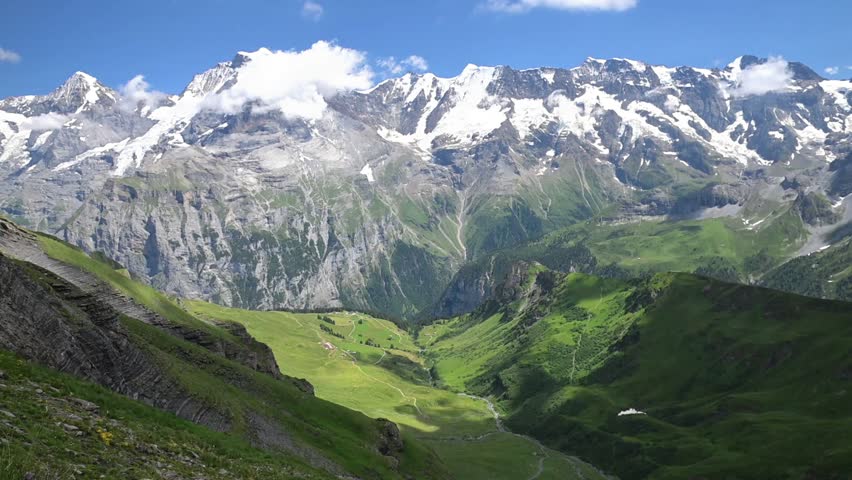Dramatic alpine panorama of snow-covered peaks, rugged cliffs and lush green meadows near Birg in the Swiss Alps.