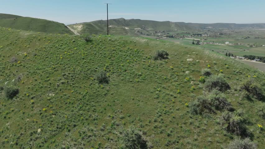 Aerial drone footage captures a scenic highway winding through lush green hills in Emmett Idaho with a flowing river and rural countryside under a clear blue sky
