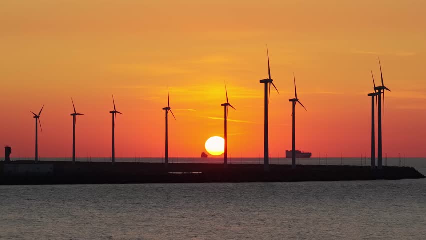 Drone view of wind turbines against a vibrant sunset. Silhouettes of wind turbines. Green renewable energy and wind farm technology at dusk.