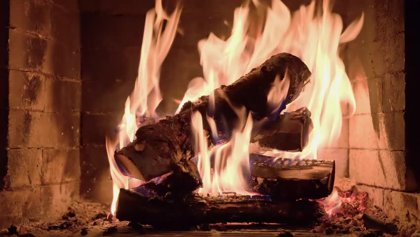 Burning wooden logs with flames and hot glowing embers inside a home fireplace. Cozy winter atmosphere and warm fire indoors.