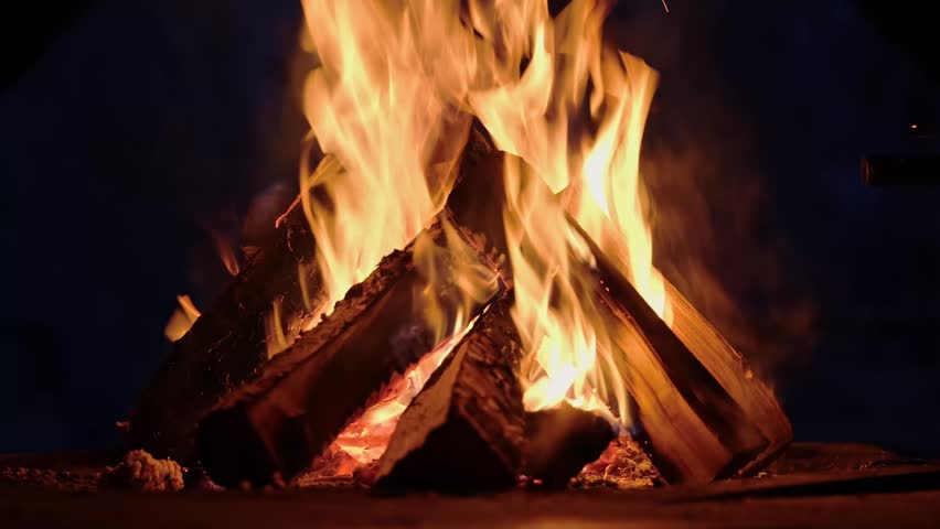 Burning wooden logs with flames and hot glowing embers inside a home fireplace. Cozy winter atmosphere and warm fire indoors.