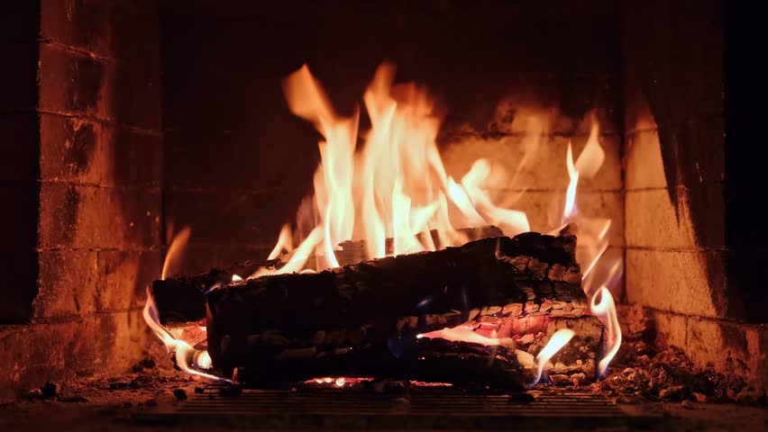 Burning wooden logs with flames and hot glowing embers inside a home fireplace. Cozy winter atmosphere and warm fire indoors.