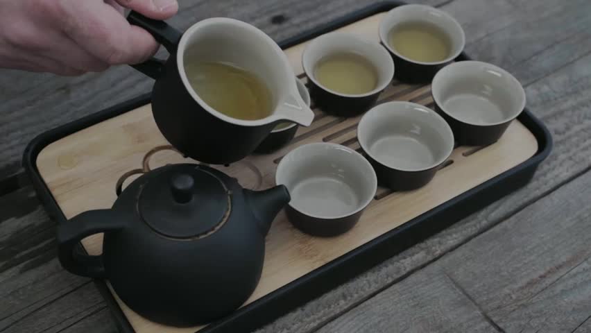 Hand pours tea into small ceramic cups. Tea set rests on wooden tray. Calm, traditional tea ceremony moment. Peaceful ritual evokes mindfulness and warmth. Great for wellness, cultural