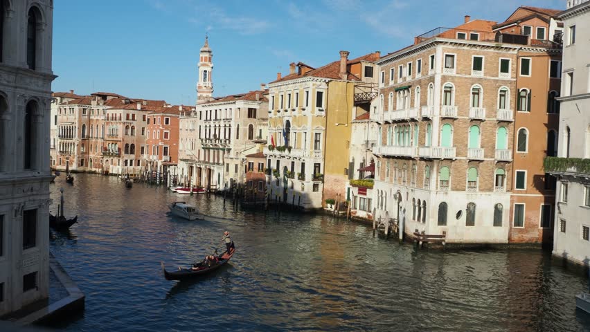 Gondola navigating through Venetian canal flanked by historic architecture - A traditional gondola glides along the water in Venice, Italy, surrounded by historic buildings and scenic canalways under clear daylight.