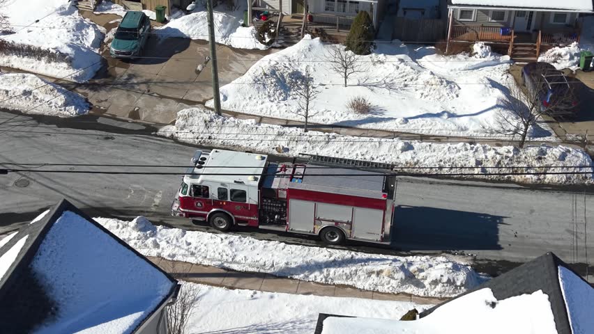 Aerial view Experience a stunning aerial perspective of a fire truck maneuvering through the winter landscape of Bichville, Nova Scotia. Snow blankets the peaceful neighborhood.