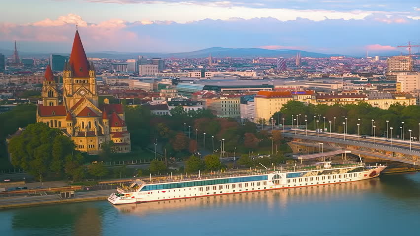 Vienna Austria skyline view featuring the historic Franz of Assisi Church, the Danube River, modern city architecture and surrounding hills during beautiful evening light.