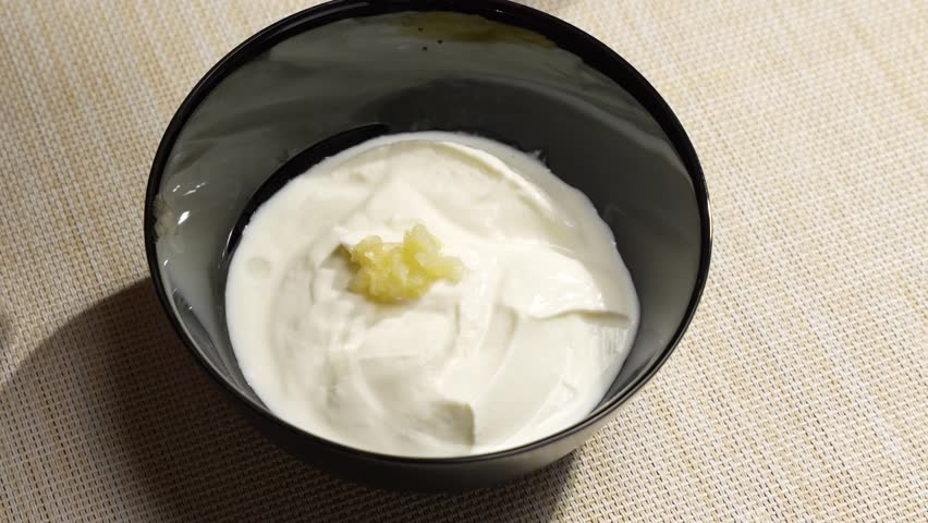Garlic and lemon juice are added to a creamy yogurt sauce in a black bowl. A close-up shows preparation of a fresh savory dip.