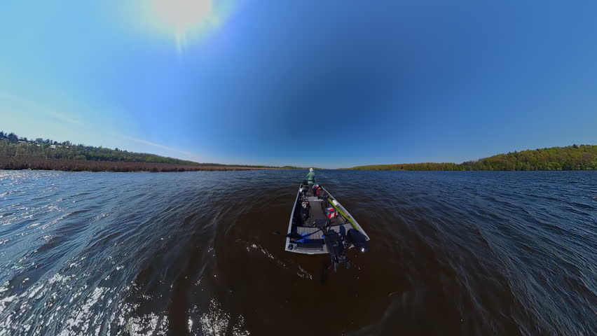 Fisherman is fishing on lake from boat casting spinning rod at daylight. Angler is standing in an equipped boat and catching fish while trolling. Man holds spinning rod while offshore during sunny day