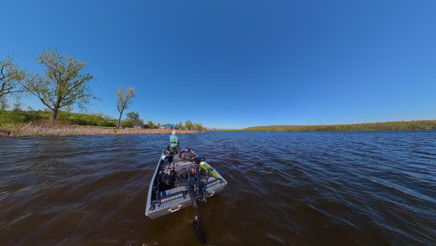 Fisherman is fishing on lake from boat casting spinning rod at daylight. Angler is standing in an equipped boat and catching fish while trolling. Man holds spinning rod while offshore during sunny day
