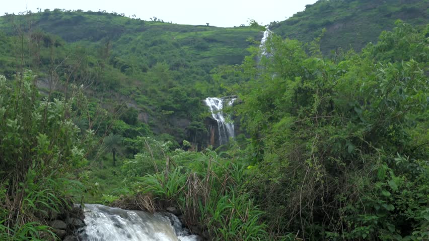 Scenic view of a lush green landscape featuring a cascading waterfall nestled amidst dense vegetation near Pune, Maharashtra, during the peak monsoon season. Monsoon is the annual rainy season in India from June to September.