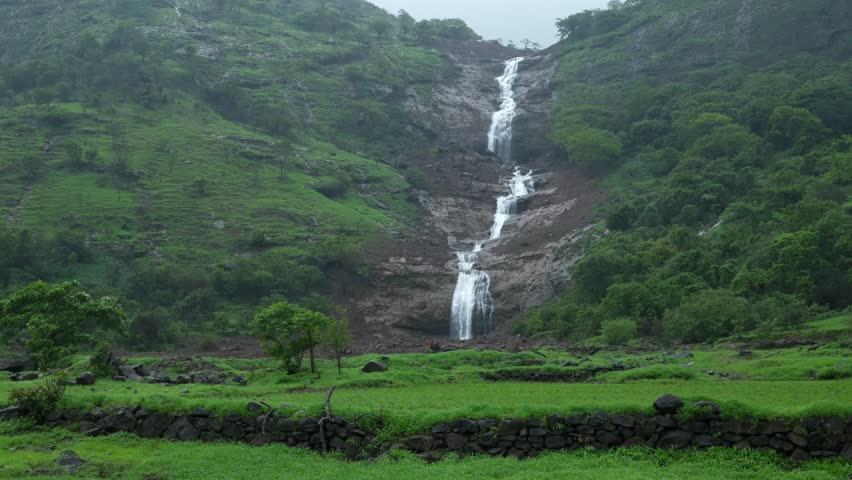 Scenic view of a lush green landscape featuring a cascading waterfall nestled amidst dense vegetation near Pune, Maharashtra, during the peak monsoon season. Monsoon is the annual rainy season in India from June to September.