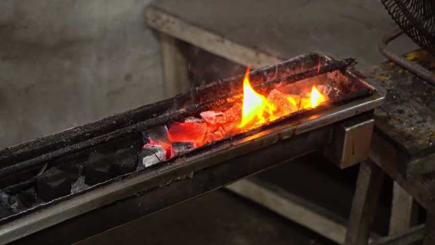Traditional Indonesian chicken satay skewered on bamboo sticks, grilling and sizzling over glowing hot charcoal coals at a local street food stall.