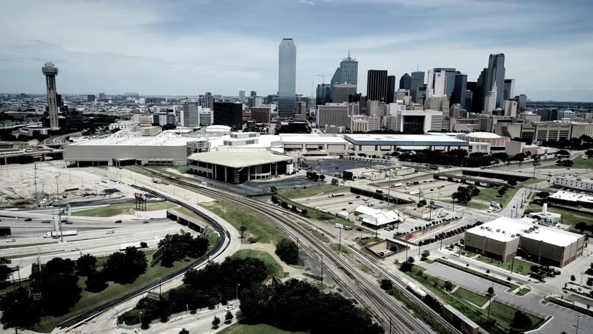 Aerial view of downtown Dallas skyline featuring busy highway traffic and railway tracks during a bright day