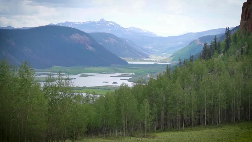 Scenic mountain valley landscape with a winding river and green aspen forest under a cloudy sky