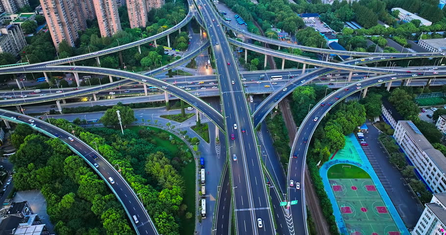 Multilevel highway interchange crossing a green urban district in Nanjing, China, showing dense traffic, elevated ramps, apartment towers, and a basketball court.