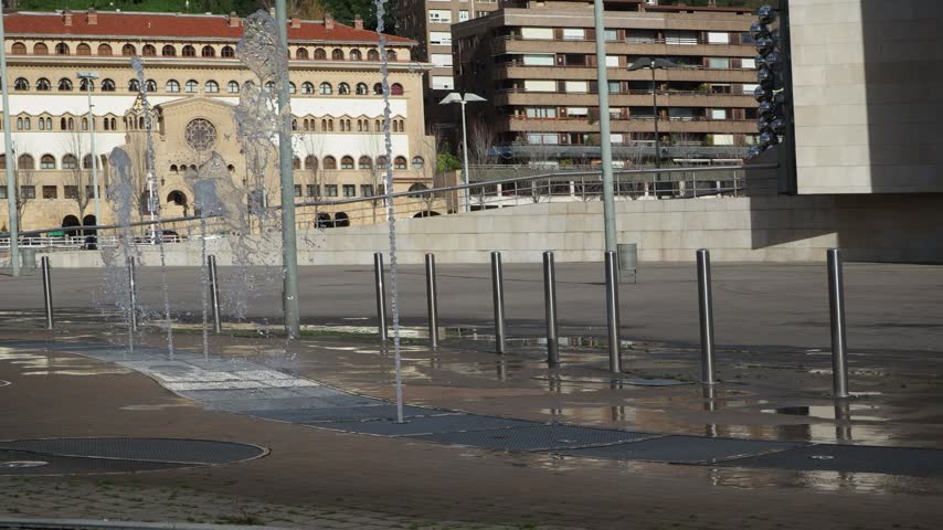 Water jets spraying from ground fountain in Bilbao plaza - Ground level fountains spraying water upwards in an urban plaza in Bilbao, surrounded by modern and historic architecture.