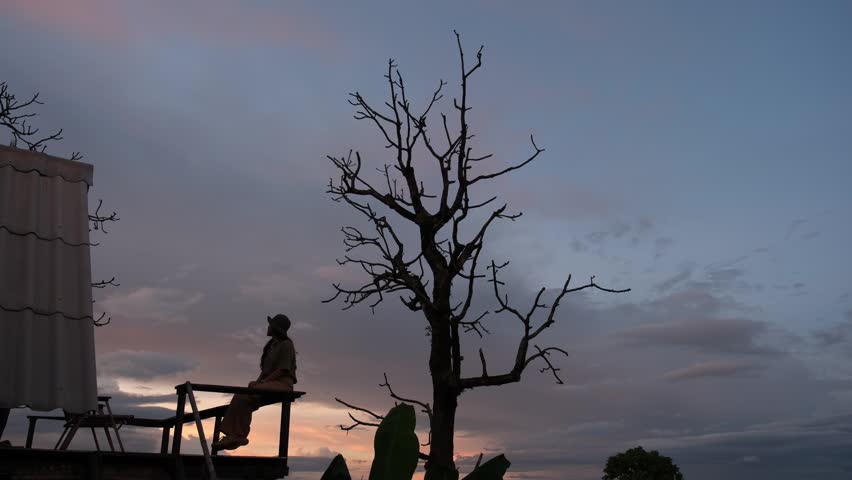 A woman sitting on wooden balcony, looking at mountain views before sunset