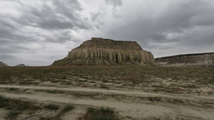 Off-road vehicle perspective captures a striking rock formation with layered cliffs and sparse vegetation under an overcast sky