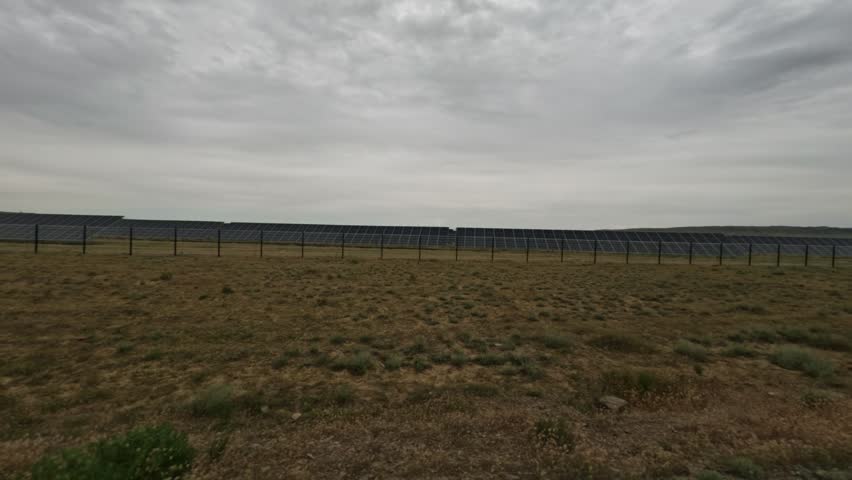 Continuous view of a solar panel field from a moving vehicle, highlighting the vast landscape and cloudy sky in the background