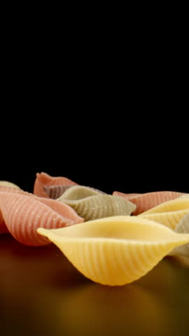 MACRO: Raw colour conchiglie pasta fall on a black table, Slow motion