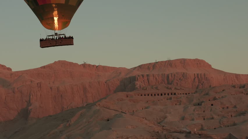 Morning hot air balloon ride in Luxor, flying over semi-rocky Deir el-Bahari complex of ancient Egyptian buildings Temple of Hatshepsut