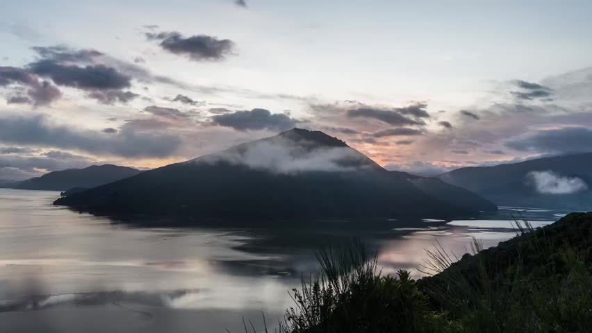 Sunset over a mountainous landscape with clouds, calm body of water, and clear sky. - LAKE TAUPO, NEW ZEALAND, May 4, 2016