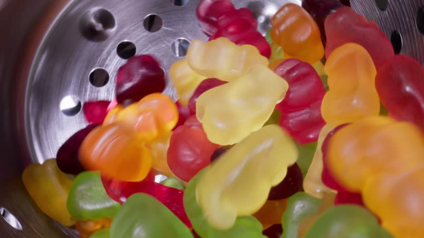 Slow motion closeup gummy bears tumbling and bouncing inside stainless steel colander into industrial conveyor, Food production.