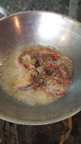Cooking traditional Pad Thai noodles with shrimp. Frying fresh prawns, stir-frying rice noodles with tamarind sauce, tofu, eggs, bean sprouts, and Chinese chives over high heat in hot cooking wok.