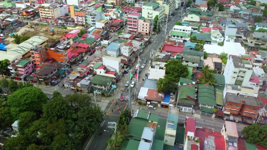 Aerial view over bustling neighborhood in Philippines showing dense residential houses colorful rooftops narrow streets and traffic moving through intersection during daylight.