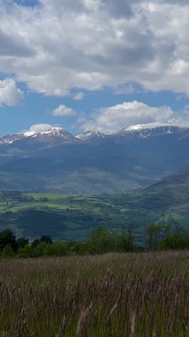 Scenic view of rolling hills, mountains, and a cloudy sky under sunlight. Mountain range with wildflowers. Landscape with Rolling Hills and Cloudy 