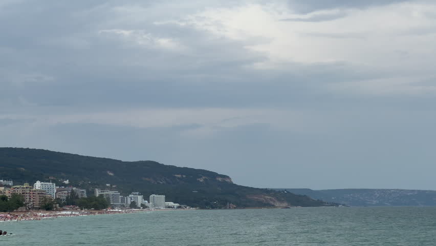 Tourists enjoying a summer day on a crowded beach under a grey, overcast sky before a storm