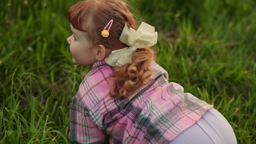 A young child lies in green grass, smiling and enjoying the moment during a sunny day in a park. Child playing in grass during sunny day in park