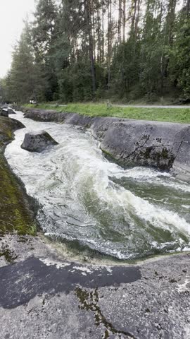 Fast flowing river water cascading through a stone canal spillway near a pine forest at sunset